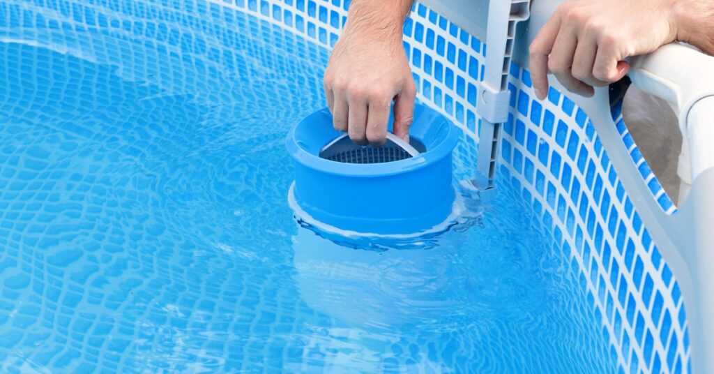Installing a blue plastic wall-mounted surface skimmer basket inside an above ground swimming pool.